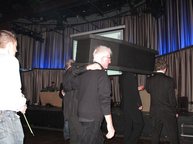 A Funeral procession down toward the stage. their holding white lillies and the coffin.